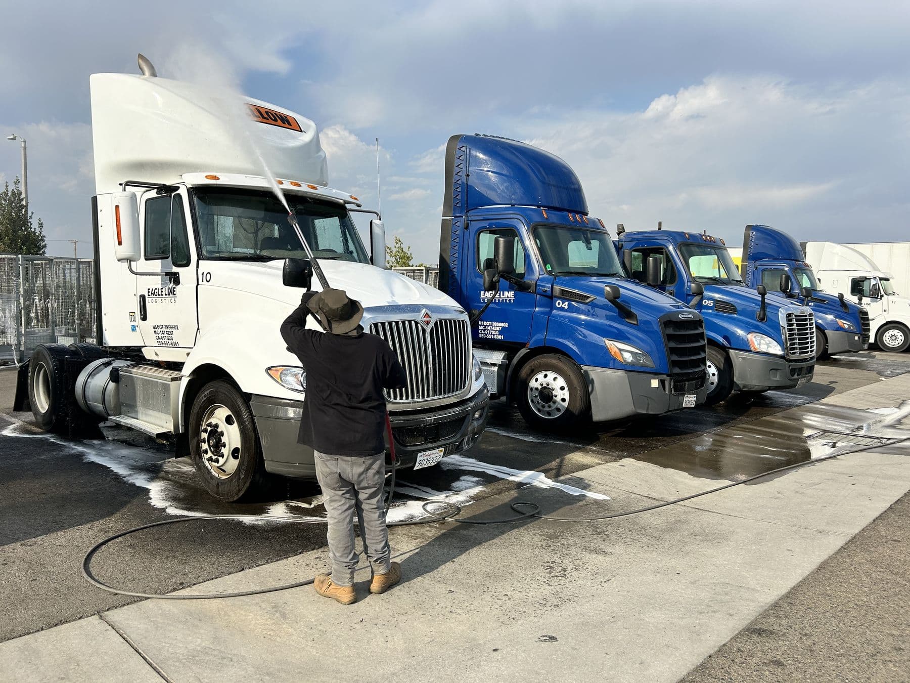 Crew member washing a semi truck in a fleet yard